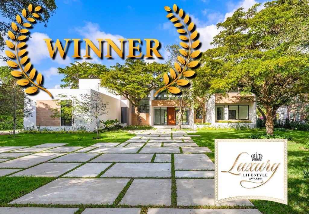 Modern luxury home with a spacious stone walkway, surrounded by greenery. Large gold WINNER text, laurel wreaths, and a Luxury Lifestyle Awards badge highlight the expertise of this architecture firm.