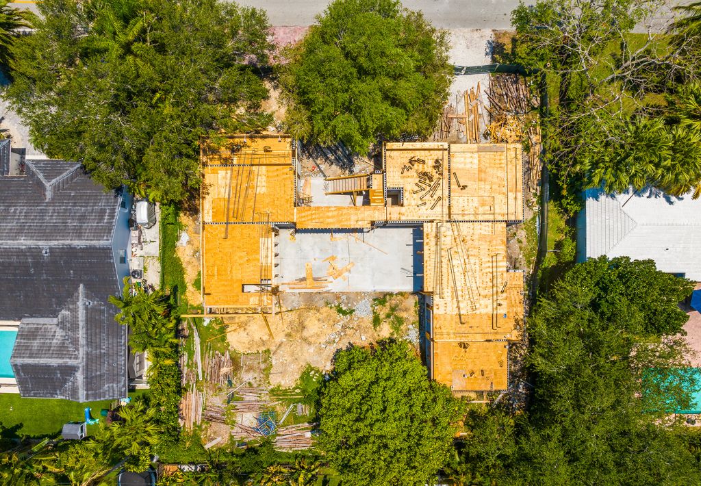Aerial view of a house under construction, surrounded by trees and neighboring homes. The wooden framework and foundation are visible, along with construction materials scattered around the site. This spatial arrangement balances the property and underscores the importance of knowing how to choose the right lot.