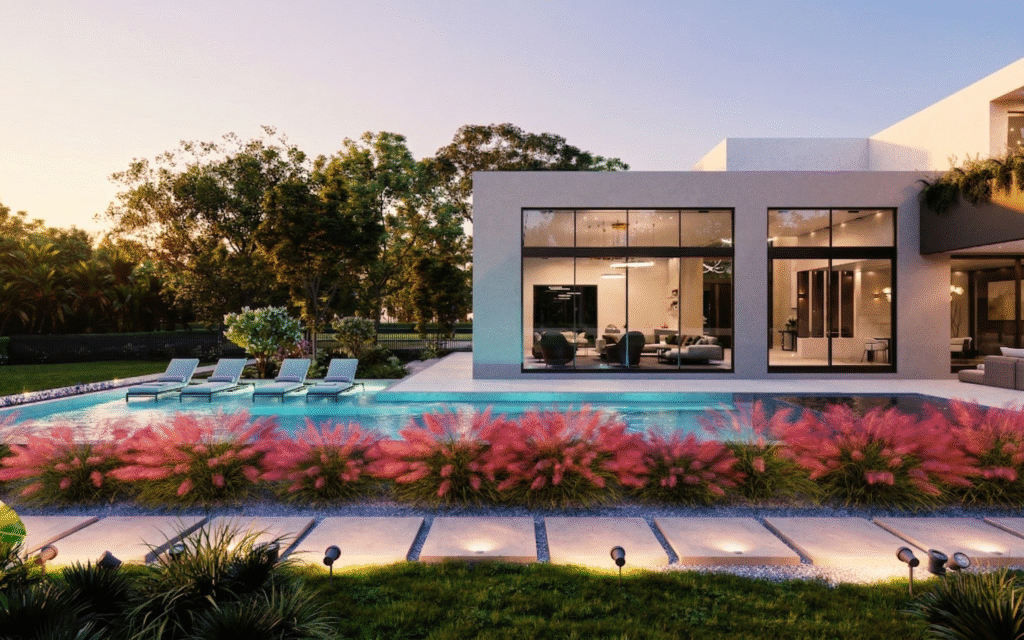 Modern ground up new construction house with large windows overlooking a backyard featuring a swimming pool, lounge chairs, pink ornamental grasses, and lush green trees under a clear sky at sunset.