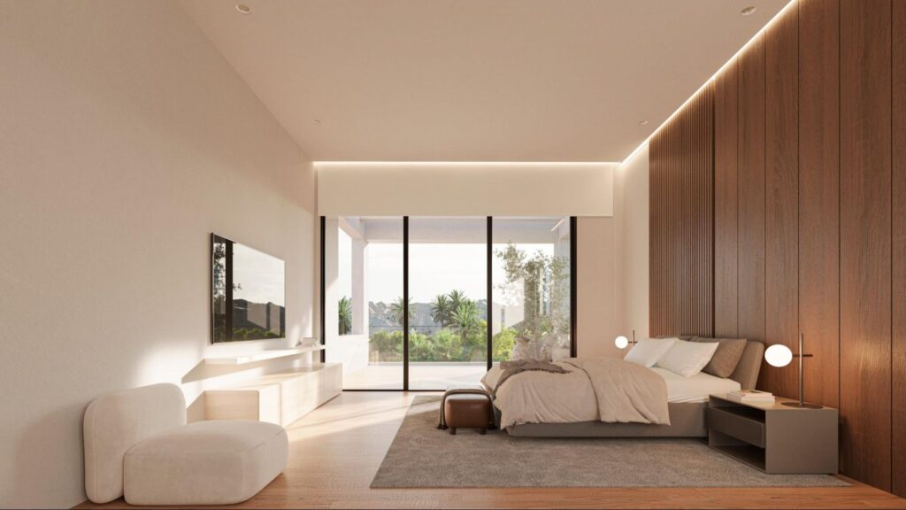 A modern bedroom with a large bed, wood accent wall, neutral furniture, and floor-to-ceiling windows overlooking greenery and a patio. Soft lighting and minimalist decor create a calm, spacious atmosphere. Elegant finishings from an Interior Designer compliment the design perfectly.