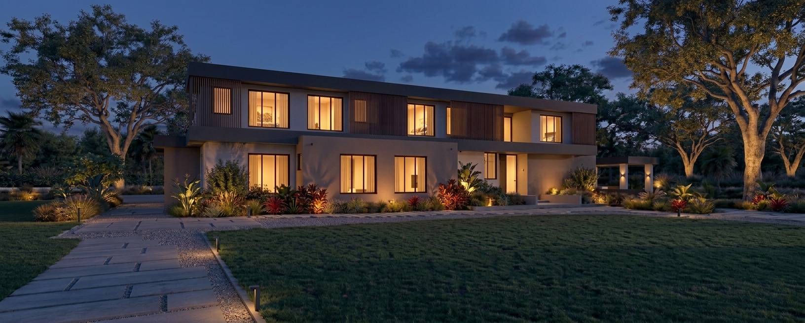 Modern two-story house with large windows warmly lit at dusk, surrounded by trees, plants, and a well-manicured lawn, with a stone pathway leading to the entrance, an exceptional example of the elegance found in luxury homes in Miami.