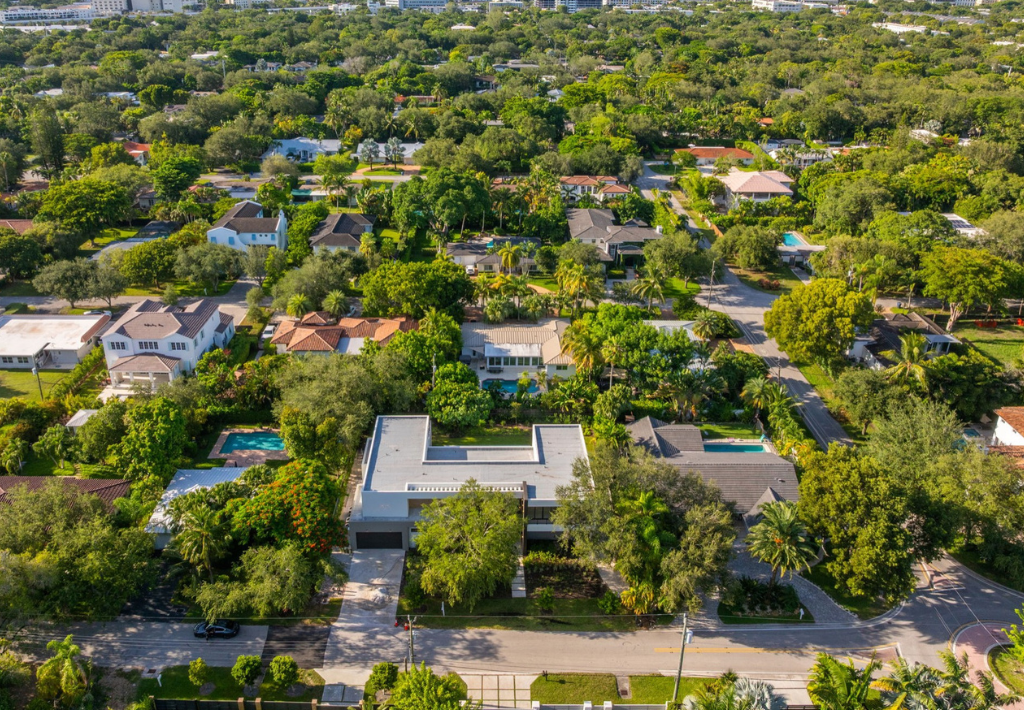 Aerial view of a suburban neighborhood with tree-lined streets, traditional and modern homes, and green yards on a sunny day.